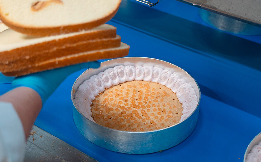 Nachdem der dünne Mürbeteigboden mit Apfelkonfitüre und seitlich mit Erdbeersahne versehen wurde, legt eine Mitarbeiterin einen Biskuitboden auf.