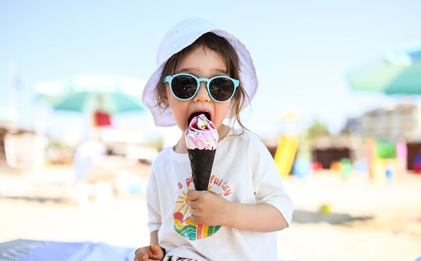 Eistester gesucht: KLeines Mädchen mit Sonnenbrille und Sonnenhut schleckt an einem Eis.