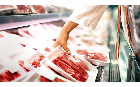 Closeup side view of unrecognizable woman chossing some fresh meat at local supermarket. The meat is cut into chops and packed into one pound packages. She has reached for a package of beef sirloin steaks.