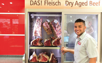 Stolz: Anis Chaabane, Azubi im dritten Lehrjahr, zeigt den Reifeschrank für Dry-aged-Beef. Als weiteres Highlight aus der Fleisch- und Wurst-Abteilung ist Iberico-Schwein zu nennen.