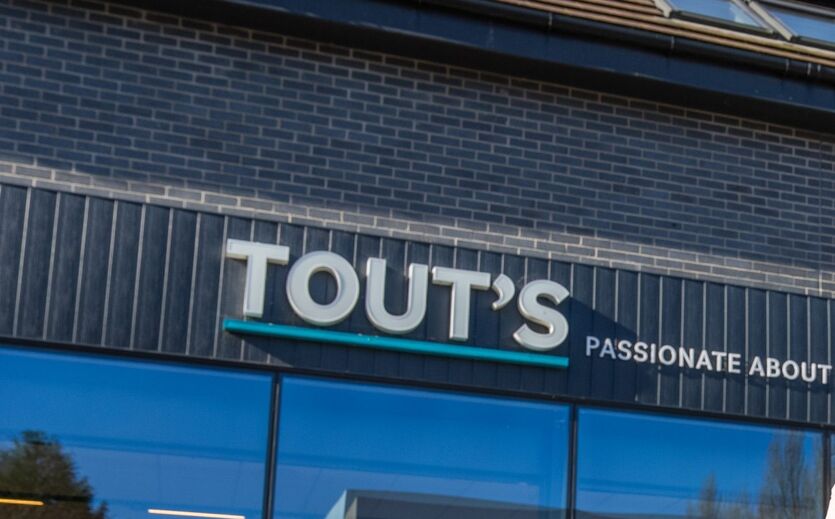 Außenansicht eines Tout’s Stores mit sichtbarem Firmenlogo.