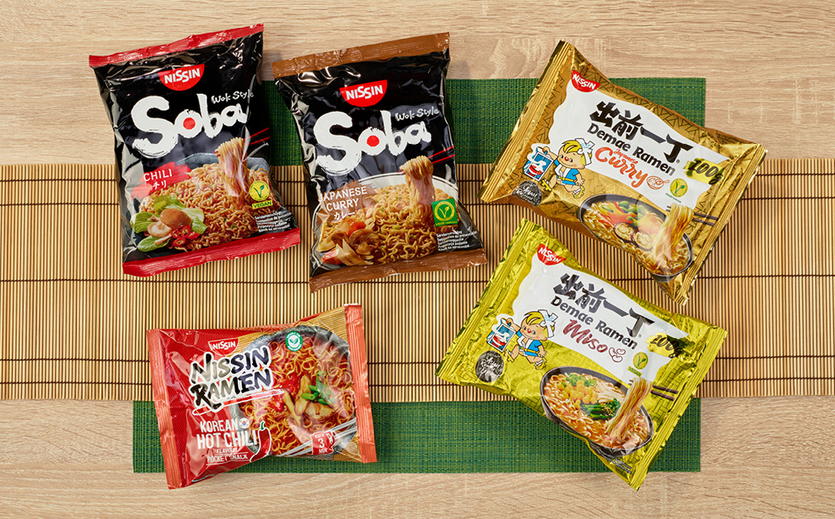 Fünf verschiedene Nissin-Instantnudelpackungen in verschiedenen Geschmacksrichtungen liegen auf einer Bambusmatte.