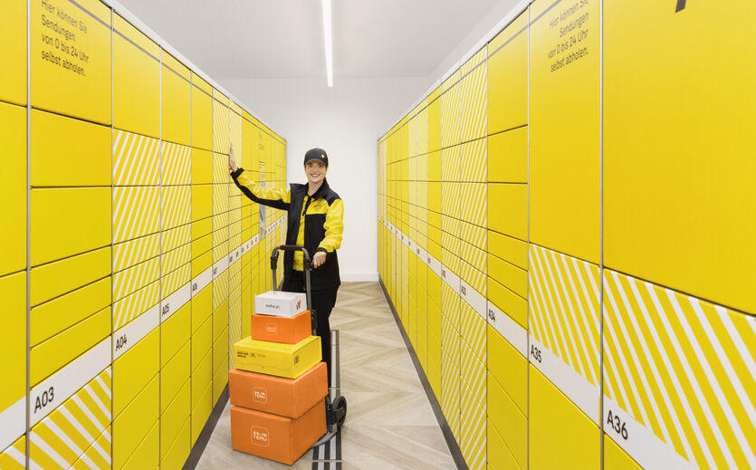 Zustellerin der Österreichischen Post steht vor gelben Paketstationen mit Temu-Paketen