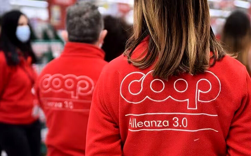 Coop Alleanza 3.0 erreicht Gewinnzone vorzeitig: Eine Mitarbeiterin mit einem roten Pulli mit dem Coop Alleanza Logo.