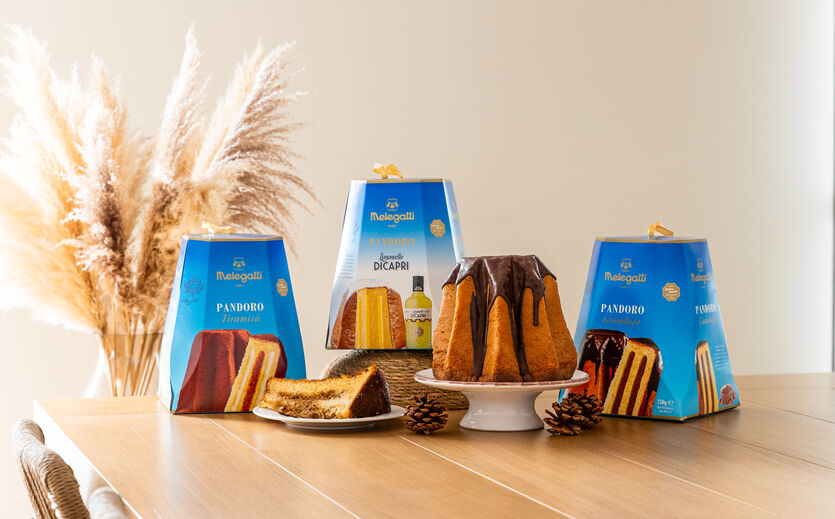 Verschiedene verpackte Melegatti-Kuchen und ein angeschnittener Pandoro mit Schokoladenglasur auf einem Tisch.