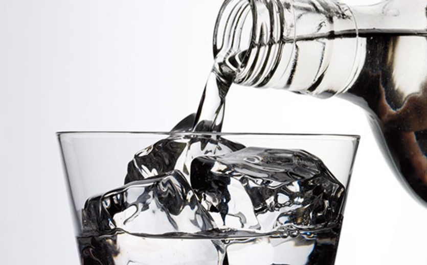 Klare Flüssigkeit wird aus einer Flasche über Eiswürfel in ein Glas gegossen.