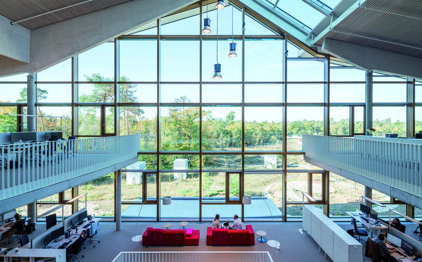 Tress-Brüder übernehmen Alnatura-Gastronomie: Foyer von oben; breite Fensterfront mit Blick nach draußen; Treppengeländer links und rechts; unten rote Sofas.n 