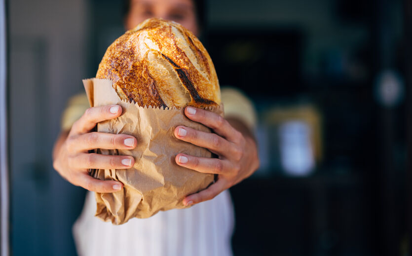 ine Person hält ein frisch gebackenes Brot in einer Papiertüte in den Händen.
