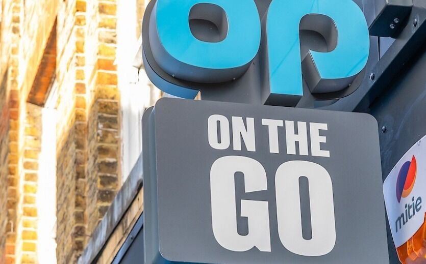 Außenaufnahme eines Co-op On-the-Go Schildes an einer Hausfassade.