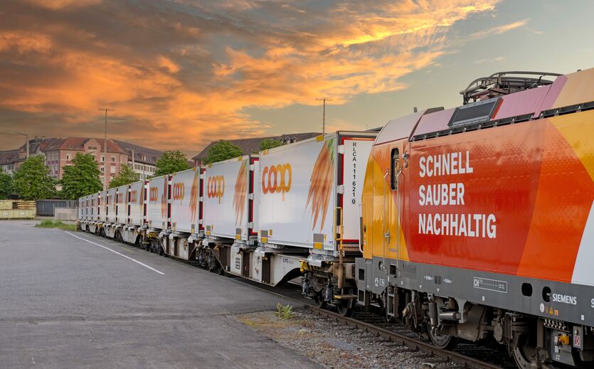 Coop-Güterzug mit Containern auf Gleisanlage bei Sonnenuntergang.