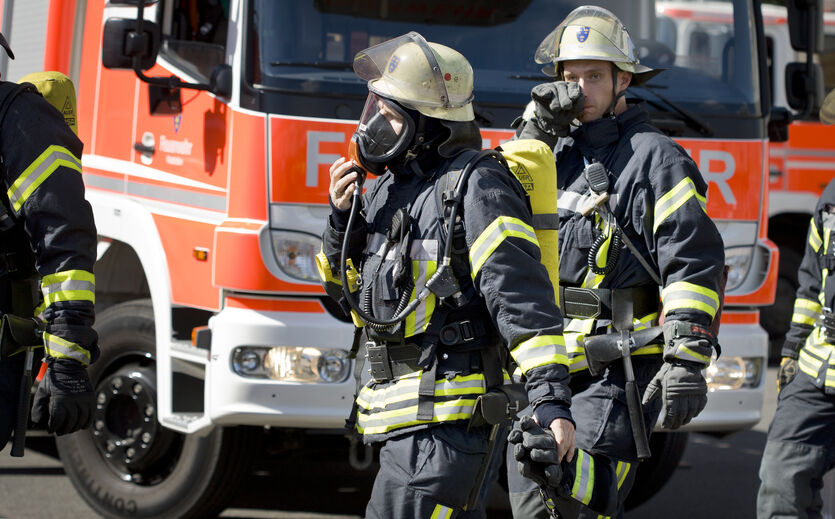 Brand bei Kölln: Zwei Feuerwehrleute in voller Montur, mit Helm und Atemschutzmaske; dahinter ein Feuerwehrfahrzeug.t