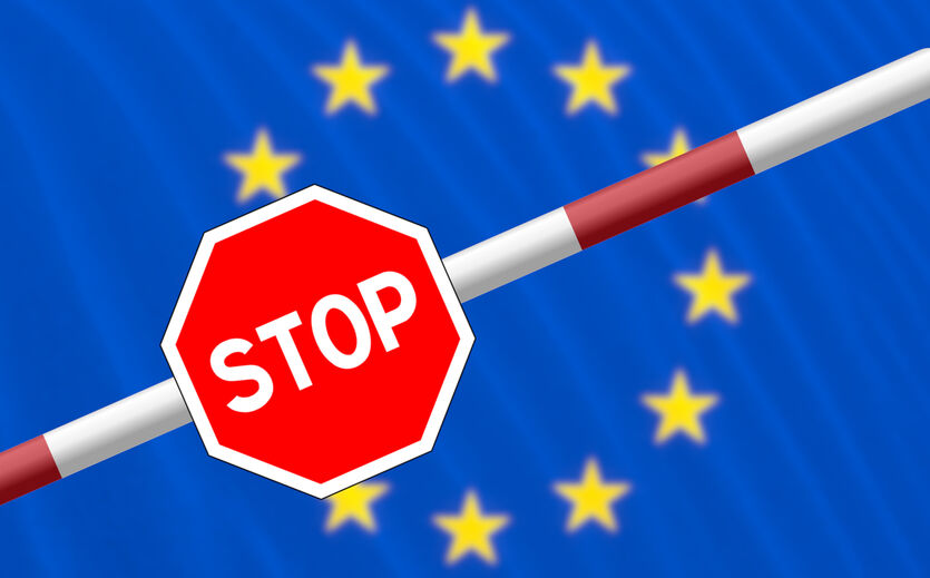 Kritik an Grenzkontrollen: Schlagbaum einer Grenze mit Stopp-Schild, dahinter Sterne der Europäischen Union auf blauem Hintergrund.e