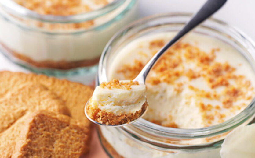 Cremiges Dessert im Glas mit Keksboden und Löffel.