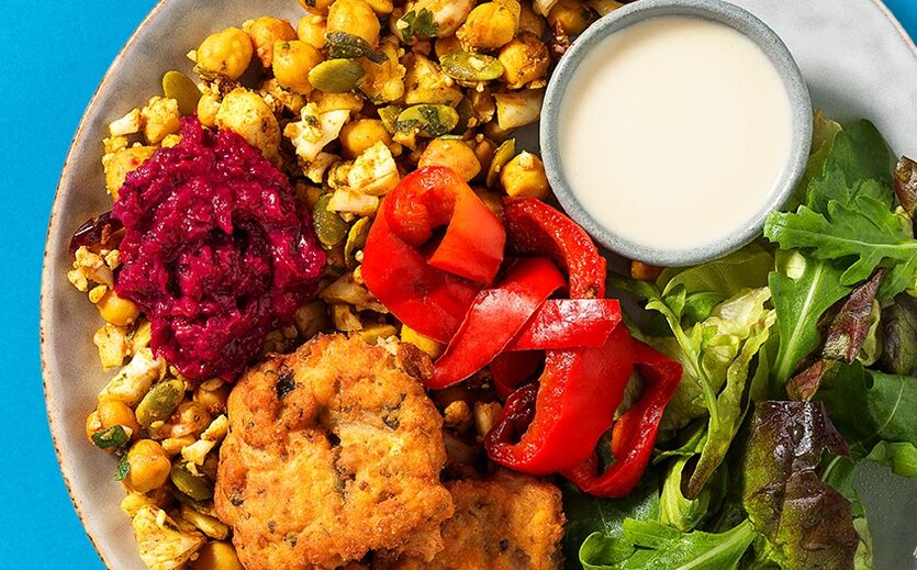 Ein Teller mit Falafel, Kichererbsen-Salat, Paprika, Blattsalat und Dip. 