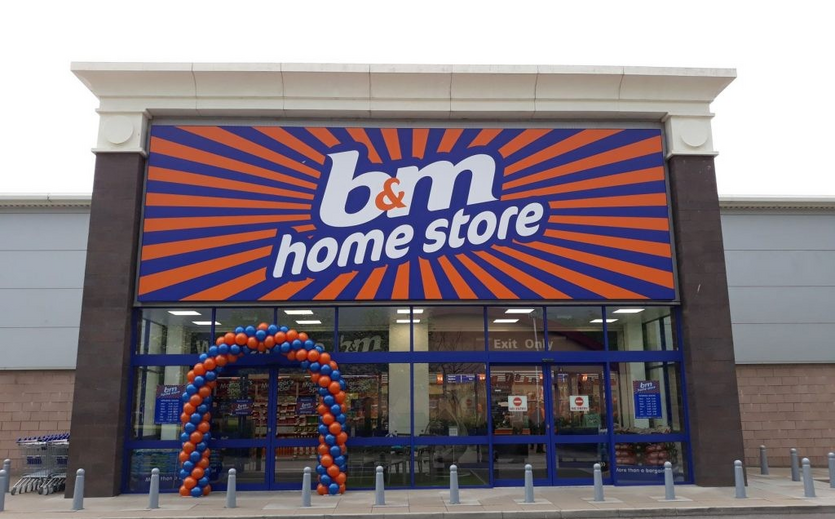 Eingangsbereich eines B&M Home Store mit orange-blauem Firmenschild und Luftballonbogen über der Tür.