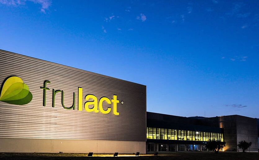 Außenansicht eines Frulact Produktionsgebäudes bei Abenddämmerung mit beleuchtetem Firmenlogo.