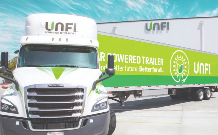 UNFI-Lkw mit grünem Solar-Trailer vor einem Distributionszentrum.