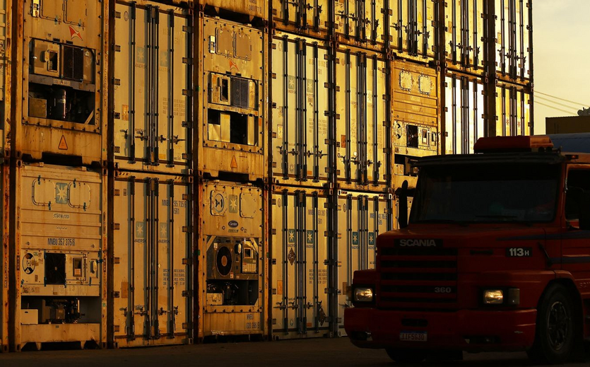 Ein roter Lkw steht vor mehreren gestapelten Frachtcontainern am Containerterminal Tecon Rio Grande im Süden Brasiliens.