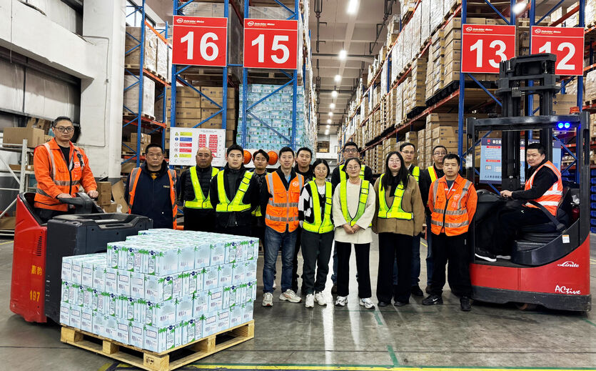 Mitarbeiterteam von Gebrüder Weiss in einer Lagerhalle mit Getränkepaletten und Hochregalen.