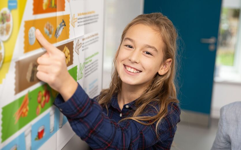Edeka.Projekt für Grundschüler: Lächelndes Mädchen zeigt auf einen Aushang.