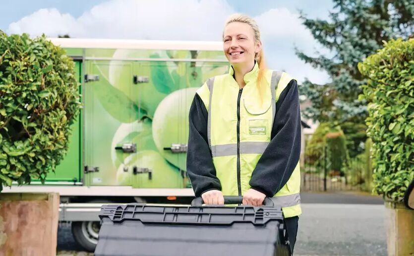 Asda setzt bei Online-Lieferung künftig auf Ocado-Technologie: Eine Frau in einer gelben Warnweste liefert in einer schwarzen Kiste eine Bestellung aus.