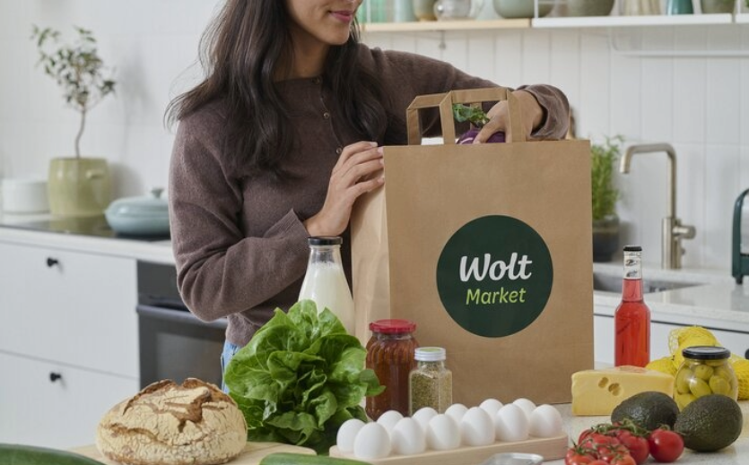 Online-Bio-Supermarkt: Frau packt in einer Küche eine Wolt-Tüte aus; vor ihr liegen diverse unverpackte Lebensmittel. 