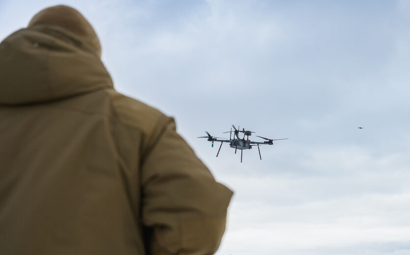 Bitkom-Umfrage: Drohne fliegt am Himmel; im Vordergrund Mann im Parka, mit Rücken der Kamera zugewandt.