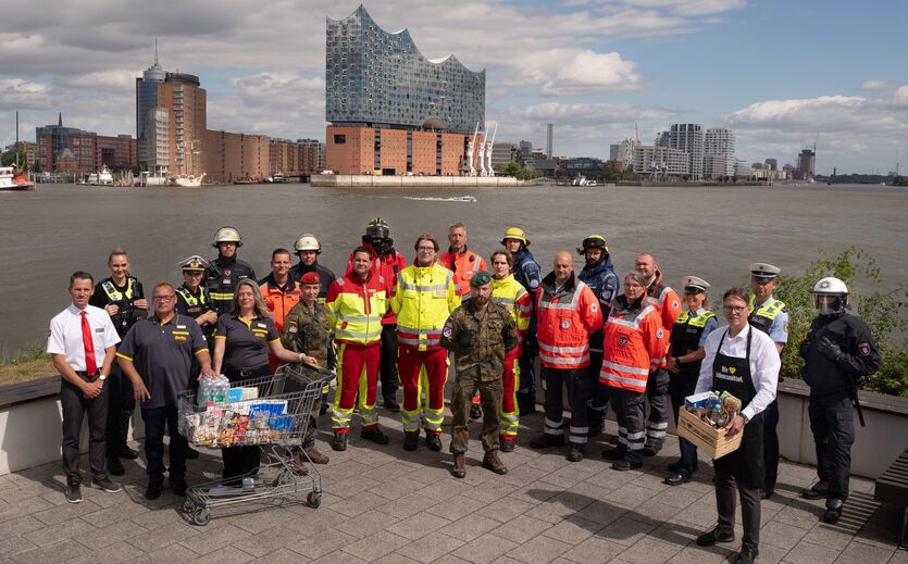 Edeka-Verbund beteiligt sich an Bundeswehr-Übung: zahlreiche Personen, zum Teil in Uniformen, haben sich aufgereiht; im Hintergrund die Hamburger Elbphilharmonie.