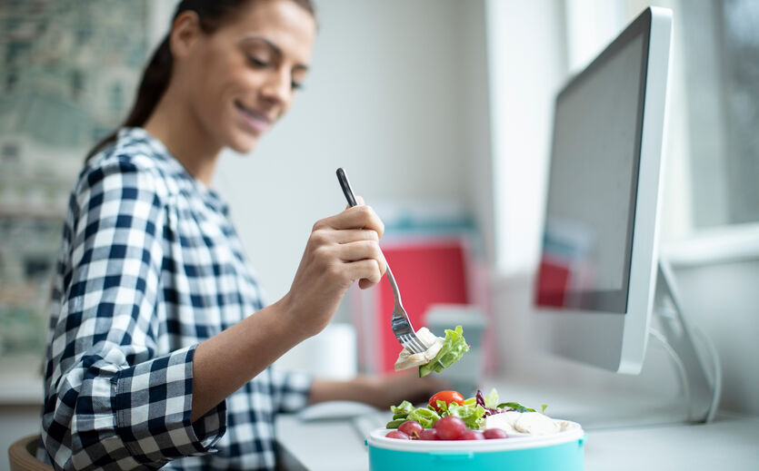 Sodexo-Studie: Frau steckt Gabel in Salat, im Hintergrund ein Bildschirm.