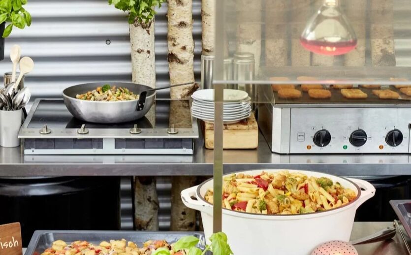 Personalie Frosta Foodservice: Schüssel mit Essen, dahinter Herde und Kochplatten mit weiteren Lebensmittelprodukten.