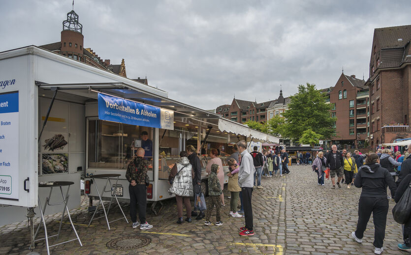 Öffnungszeiten beim Hamburger Fischmarkt: Marktstände; Kunden in einer Schlange vor einem Wagen; Passanten sind unterwegs. 