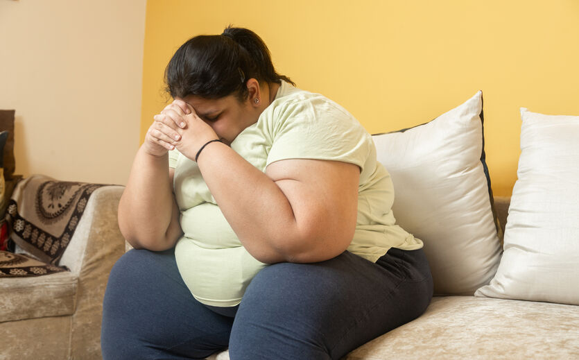 Abnehmtablette kommt: Dicke Frau sitzt auf einem Sofa.