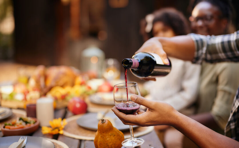 Weinexportzahlen: Person gießt sich ein Glas Rotwein ein; im Hintergrund eine Tafelrunde.n