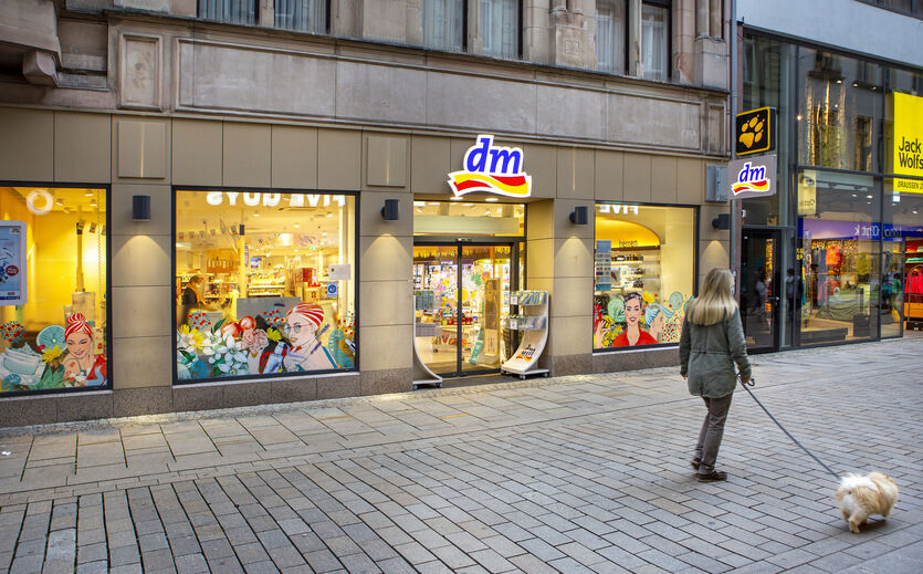 Zukunftsfähigkeit von dm: Außenaufnahme einer dm-Filiale in einer Fußgängerzone; mit Passantin.