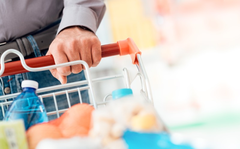 Man doing grocery shopping at the supermarket, he is pushing a full trolley, hand detail close up